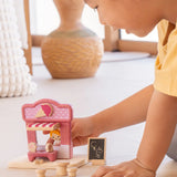 Child playing with the PlanToys ice cream shop wooden toy playset holding the wooden worker figure at the serving window of the shop.