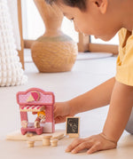 Child playing with the PlanToys ice cream shop wooden toy playset holding the wooden worker figure at the serving window of the shop.