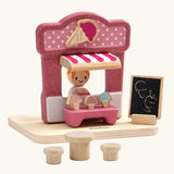 PlanToys ice cream shop wooden toy playset. Pink wooden shop with three ice cream cones, advert board, table and two seats and a worker figure.