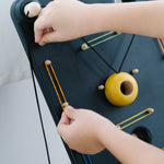 Close up of a child's hands pulling on a rubber band to attach to the PlanToys wooden wall ball game