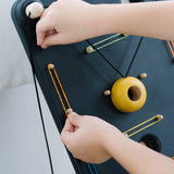Close up of a child's hands pulling on a rubber band to attach to the PlanToys wooden wall ball game