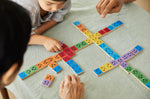 Close up of a family sat around the PlanToys rainbow wooden mood dominos game on a grey tablecloth