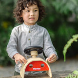 Child playin the the PlanToys Driving Console wooden toy outdoors, holding onto the wing mirror on the side.