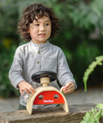 Child playin the the PlanToys Driving Console wooden toy outdoors, holding onto the wing mirror on the side.