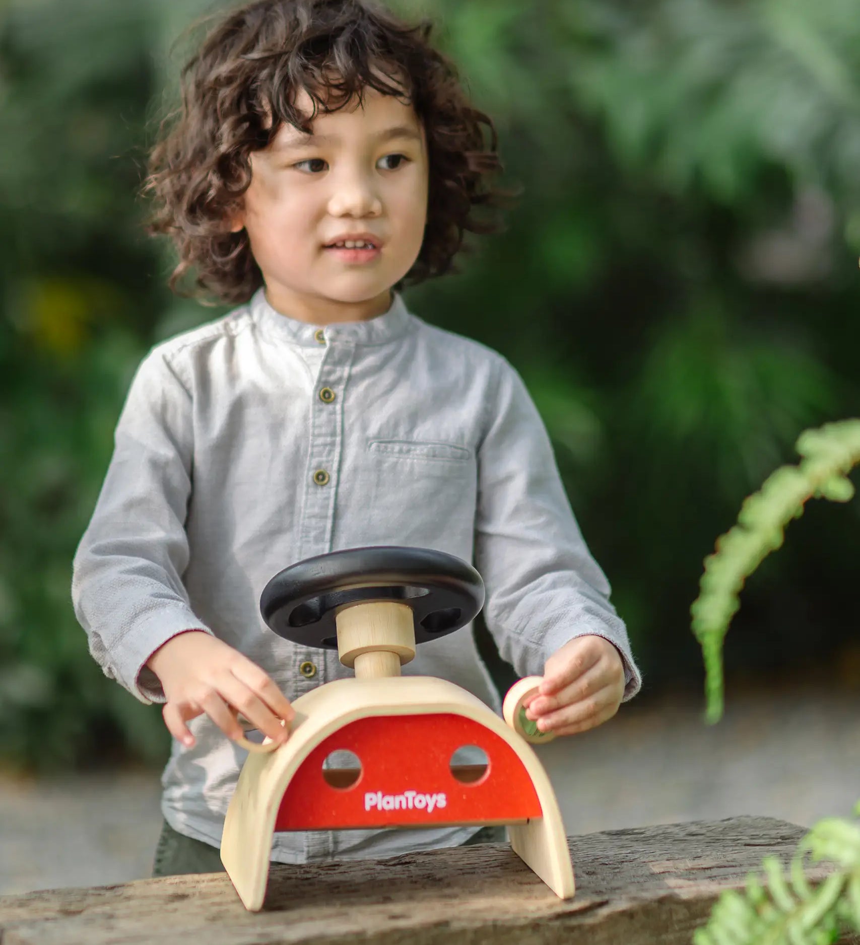 Child playin the the PlanToys Driving Console wooden toy outdoors, holding onto the wing mirror on the side.