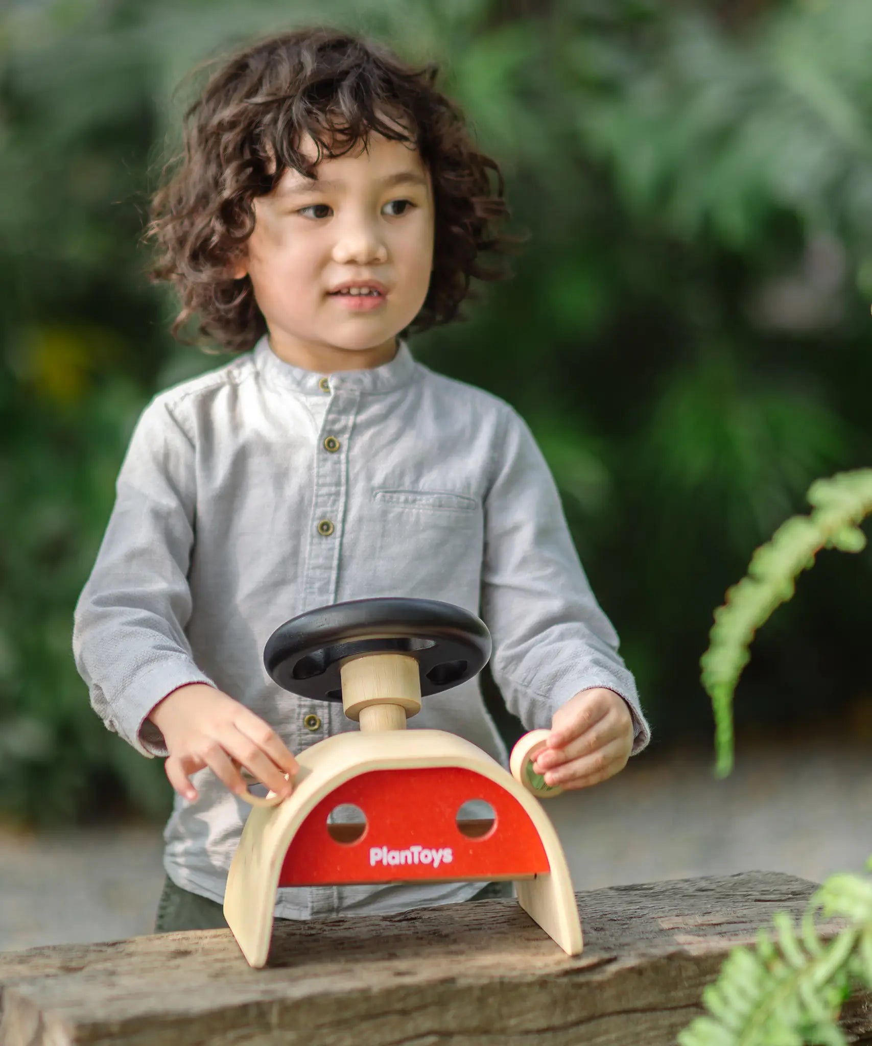 Child playin the the PlanToys Driving Console wooden toy outdoors, holding onto the wing mirror on the side.