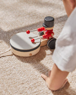 Close up of the PlanToys kids pull along drummer toy on a beige carpet next to a childs hand
