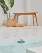 PlanToys plastic-free sailing boat bath toy in some water in front of a wooden bench