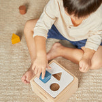 Close up of a child putting a blue wooden cube toy into the PlanToys plastic-free orchard shape sorter