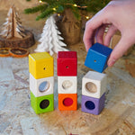 Close up of a hand placing a blue block on top of a stack of PlanToys children's toy activity blocks