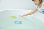 Girl reaching out to touch a PlanToys natural rubber boat toy in a bath tub