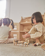 Two children sat on the floor playing with the PlanToys wooden Victorian furniture dollhouse set