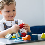 Close up of a child sat down threading PlanToys wooden lacing blocks onto a string