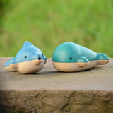 PlanToys Wooden Dolphin Whistle Toy next to the Whale Whistle on a stone wall with grass background.