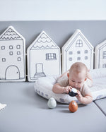 Baby laying on a white cushion looking at the PlanToys wobbly walrus