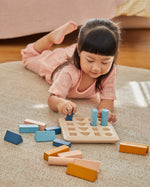 Girl laying down on a carpet placing shapes into the PlanToys plastic-free wooden shape sorter
