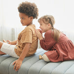 Two children on a grey sofa, the girl id playfully smiling. 