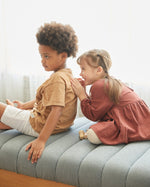 Two children on a grey sofa, the girl id playfully smiling. 