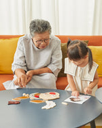 Woman and young girl playing with the PlanToys wooden build a face toy set on a wooden table