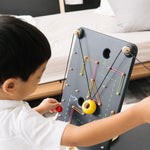 Close up of a child pulling the strings on the PlanToys wall ball game to make the ball move up the board.