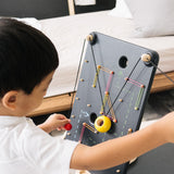 Close up of a child pulling the strings on the PlanToys wall ball game to make the ball move up the board.