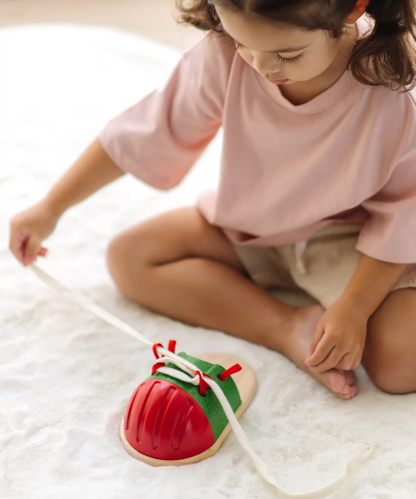 Child tying the laces on the PlanToys life size tie-up wooden shoe toy. 