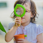 A child holding the Plan Toys Leaf Magnifier up to their eye. 