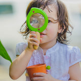 A child holding the Plan Toys Leaf Magnifier up to their eye. 