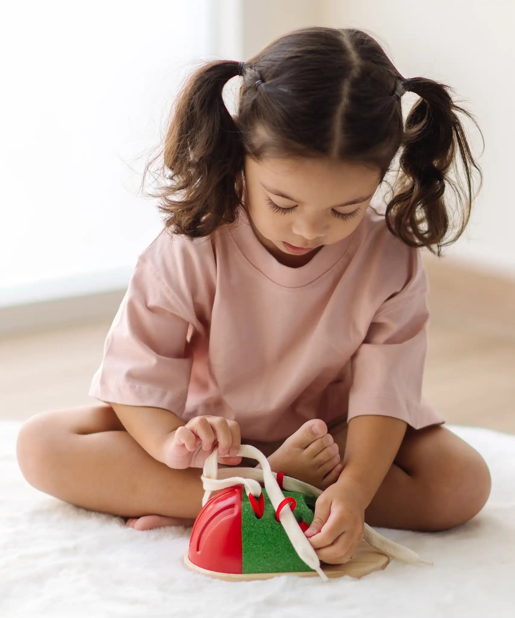 Child tying the laces on the PlanToys life size tie-up wooden shoe toy. 