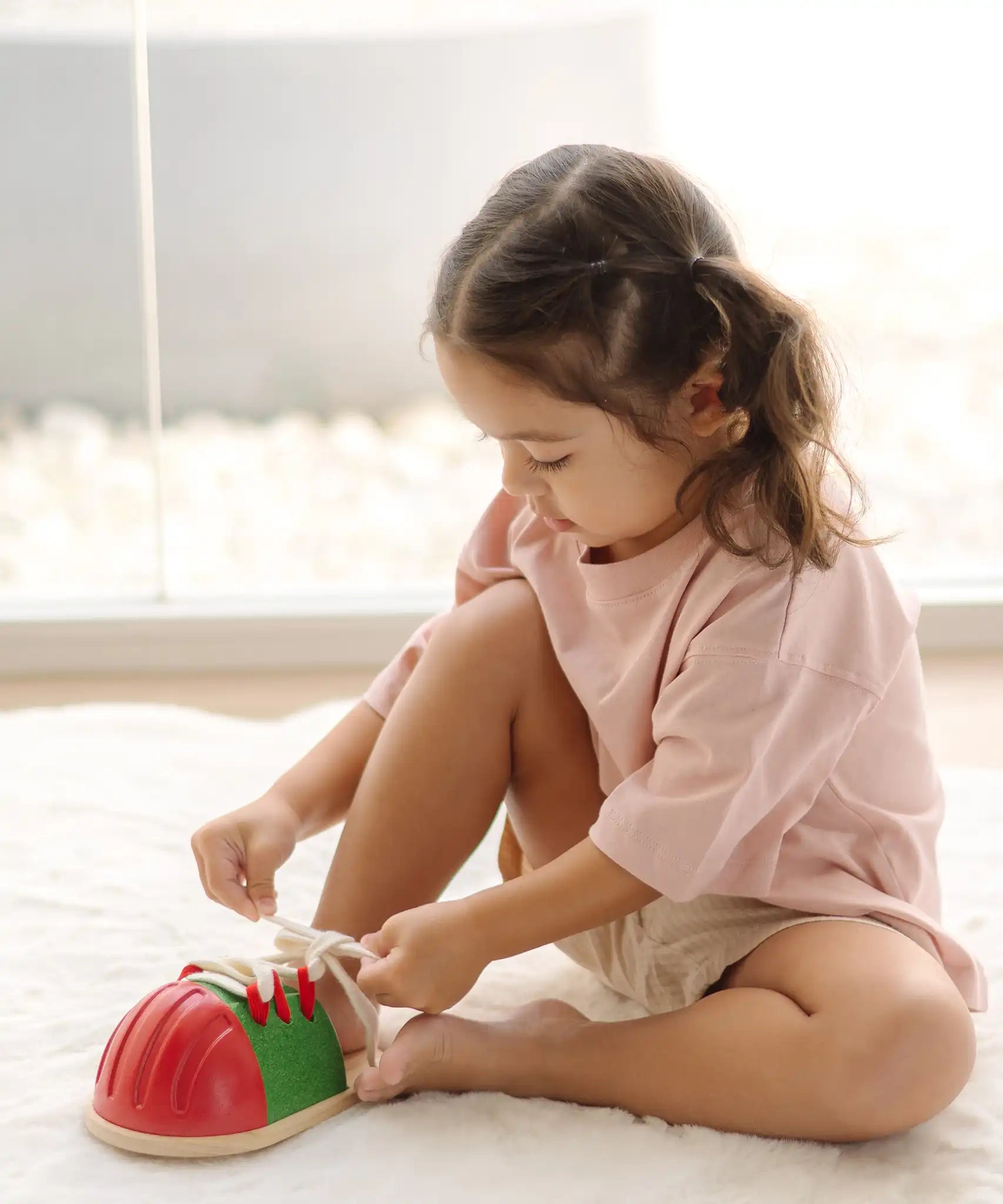 Child tying the laces on the PlanToys life size tie-up wooden shoe toy. 