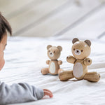 A PlanToys Bear next to the smaller bear on a light coloured material, a child can be seen in the corner looking towards the bears.