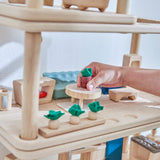 A close up of a hand playing the with Plantoys wooden living room stacked with the kitchen and bathroom set. Showing the plant pot on top of the coffee table amongst the living room accessories