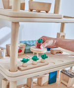 A close up of a hand playing the with Plantoys wooden living room stacked with the kitchen and bathroom set. Showing the plant pot on top of the coffee table amongst the living room accessories