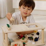 A close up of a child playing the with Plantoys wooden planspace living room showing the veg patch on top with the accessories and PlanToys dolls in the room 