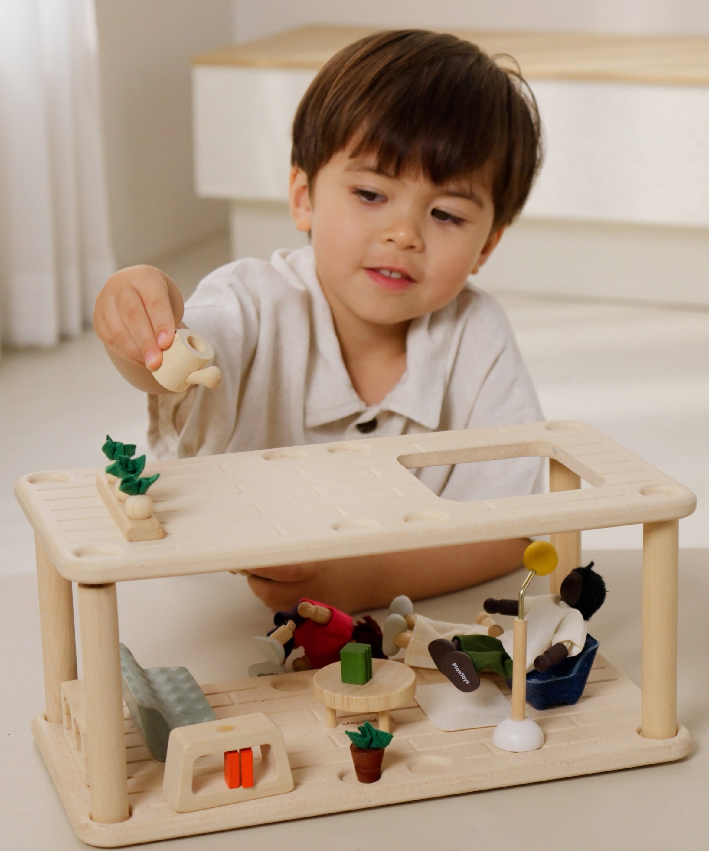 A close up of a child playing the with Plantoys wooden planspace living room showing the veg patch on top with the accessories and PlanToys dolls in the room 