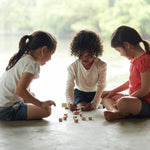 Three children sitting on the floor playing with the PlanToys Mini Memo Game set. 
