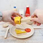 Close up of some hands holding a wooden pot of PlanToys play food honey over some toy slices of bread