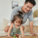 Young girl and man kneeling down looking at the PlanToys wooden baby car toy
