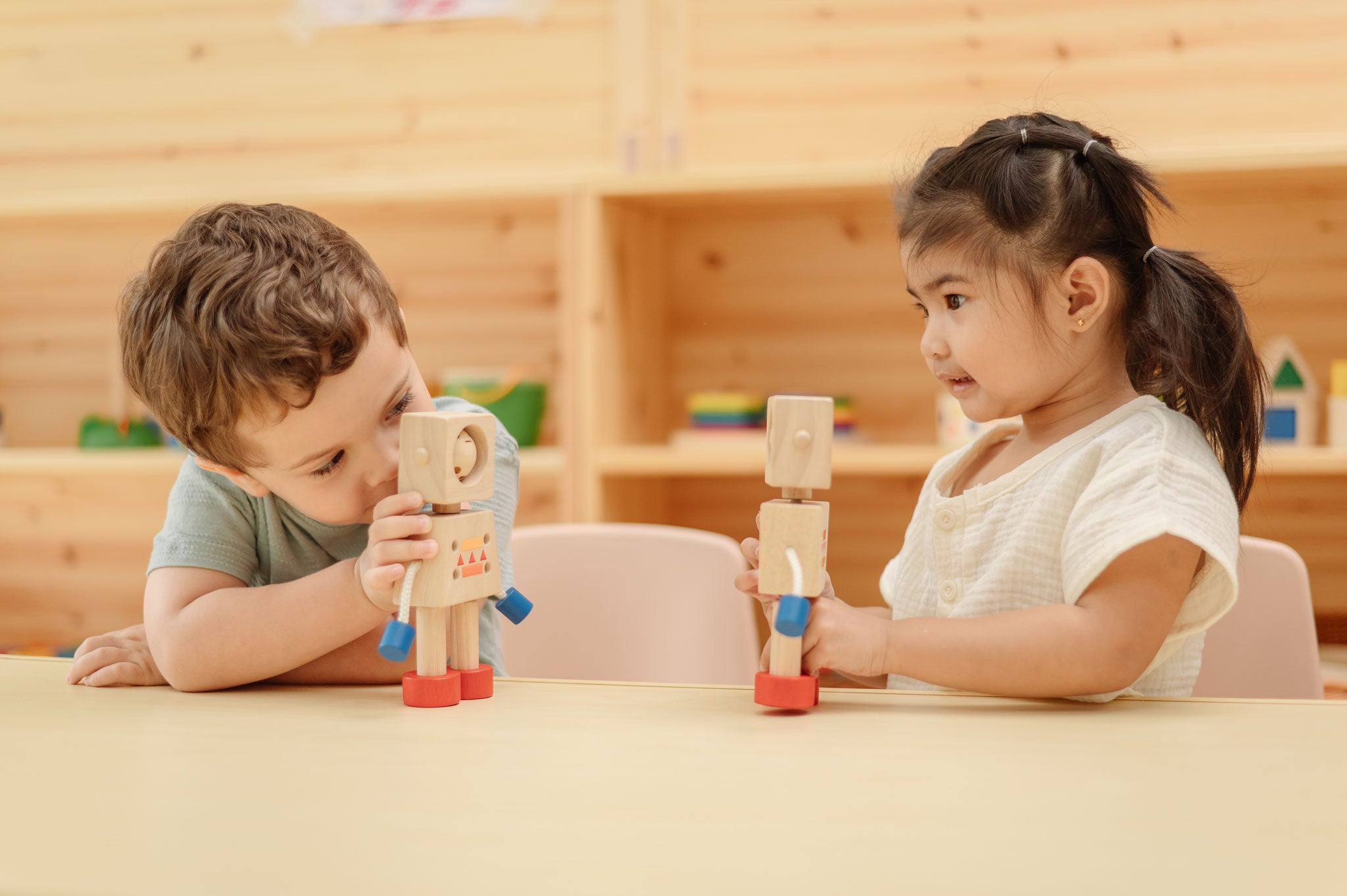 Two children sitting at a table playing with the  PlanToys Mood Bot Emotions Wooden Toy Robot. PlanToys range of toys are made from sustainably sourced rubberwood, we're proud stockists of PlanToys here at Babipur. 
