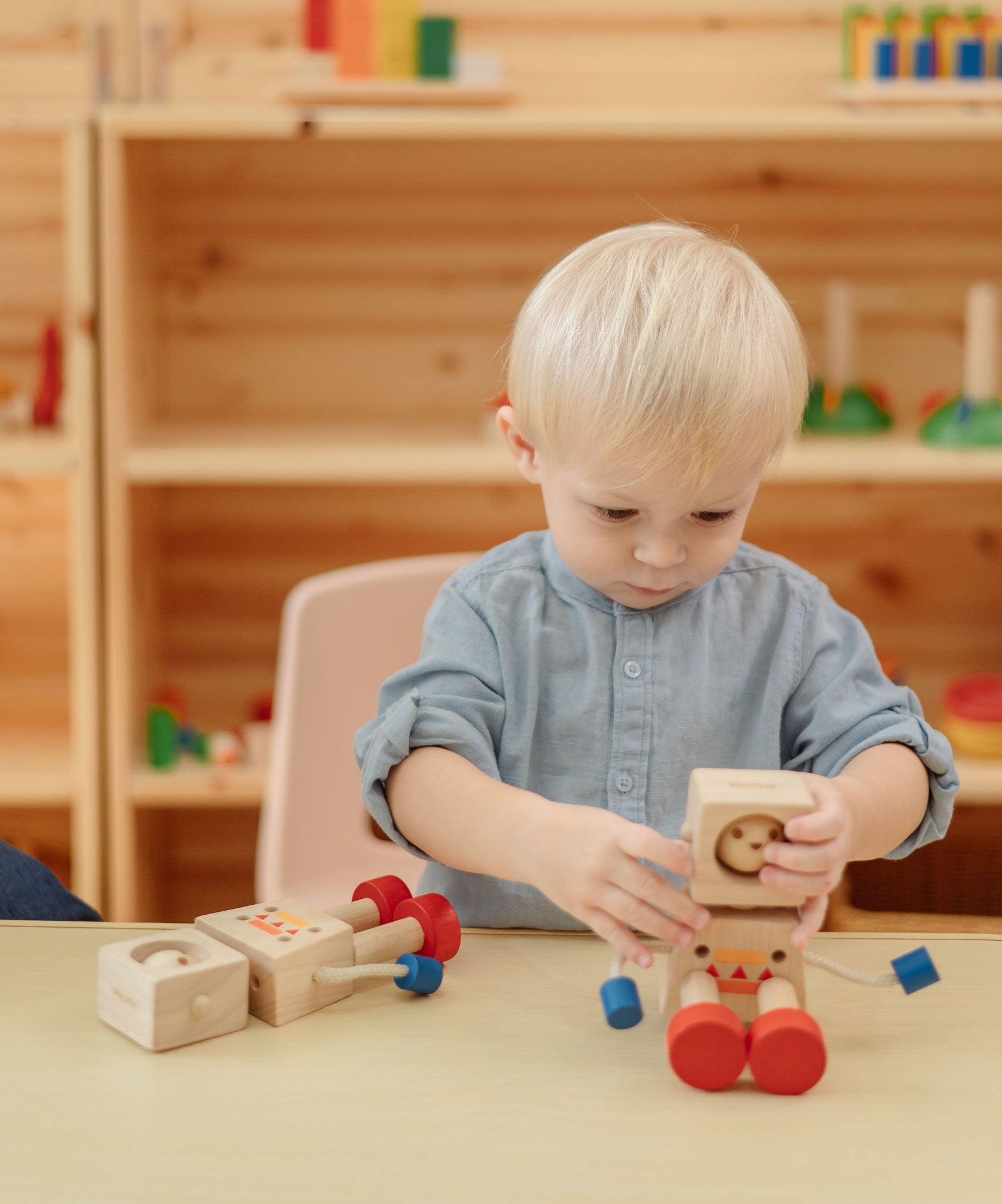 A child sitting at a table playing with the  PlanToys Mood Bot Emotions Wooden Toy Robot. PlanToys range of toys are made from sustainably sourced rubberwood, we're proud stockists of PlanToys here at Babipur. 