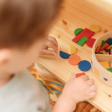 Close up of child's hands creating a colourful pattern using the wooden pieces from the PlanToys Mosaic wooden pattern making toy.