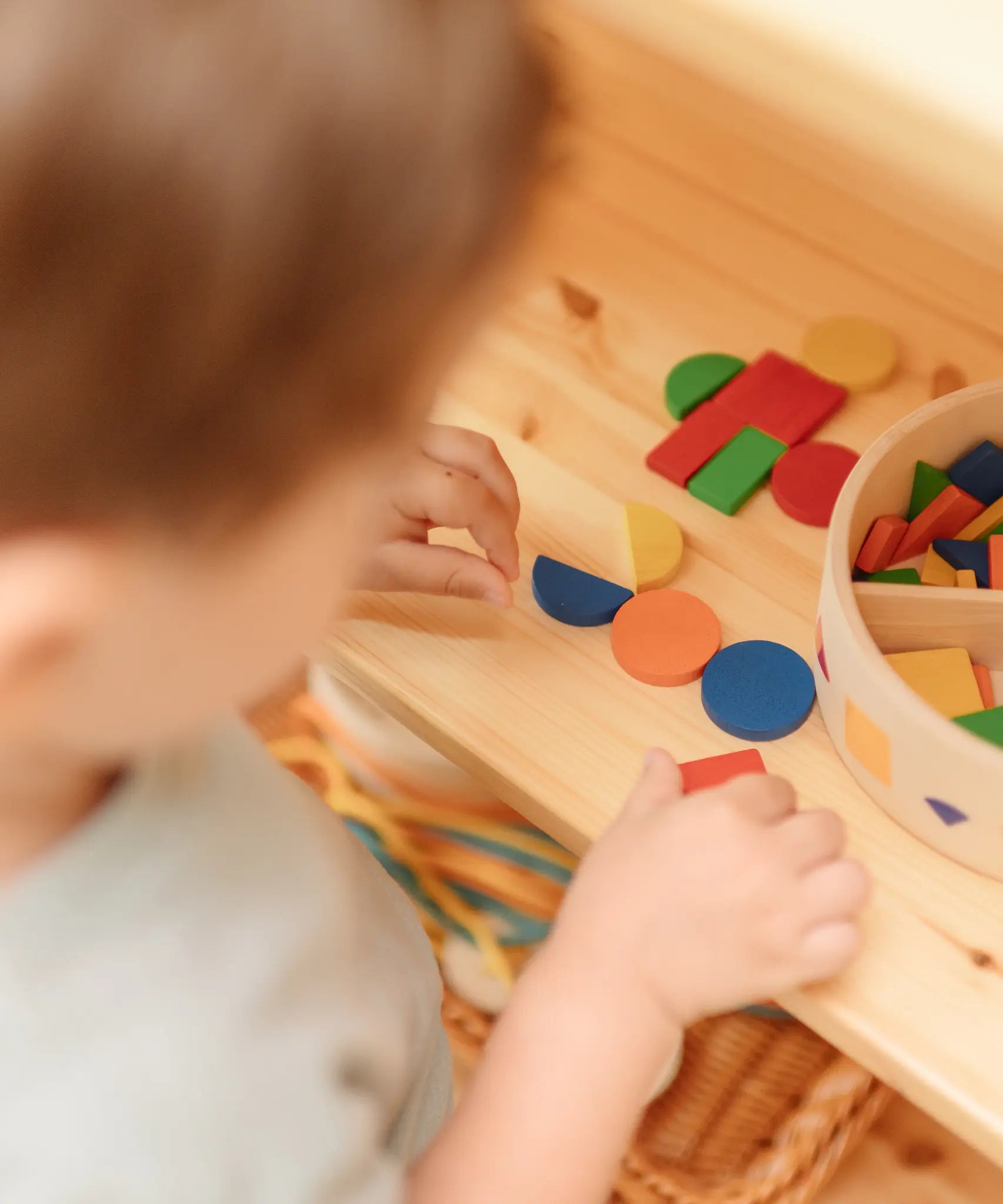 Close up of child's hands creating a colourful pattern using the wooden pieces from the PlanToys Mosaic wooden pattern making toy.