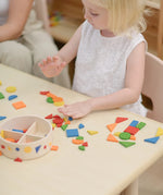 Child playing with the PlanToys mosaic wooden pattern making set taking the brightly coloured pieces out of the wooden storage tub.