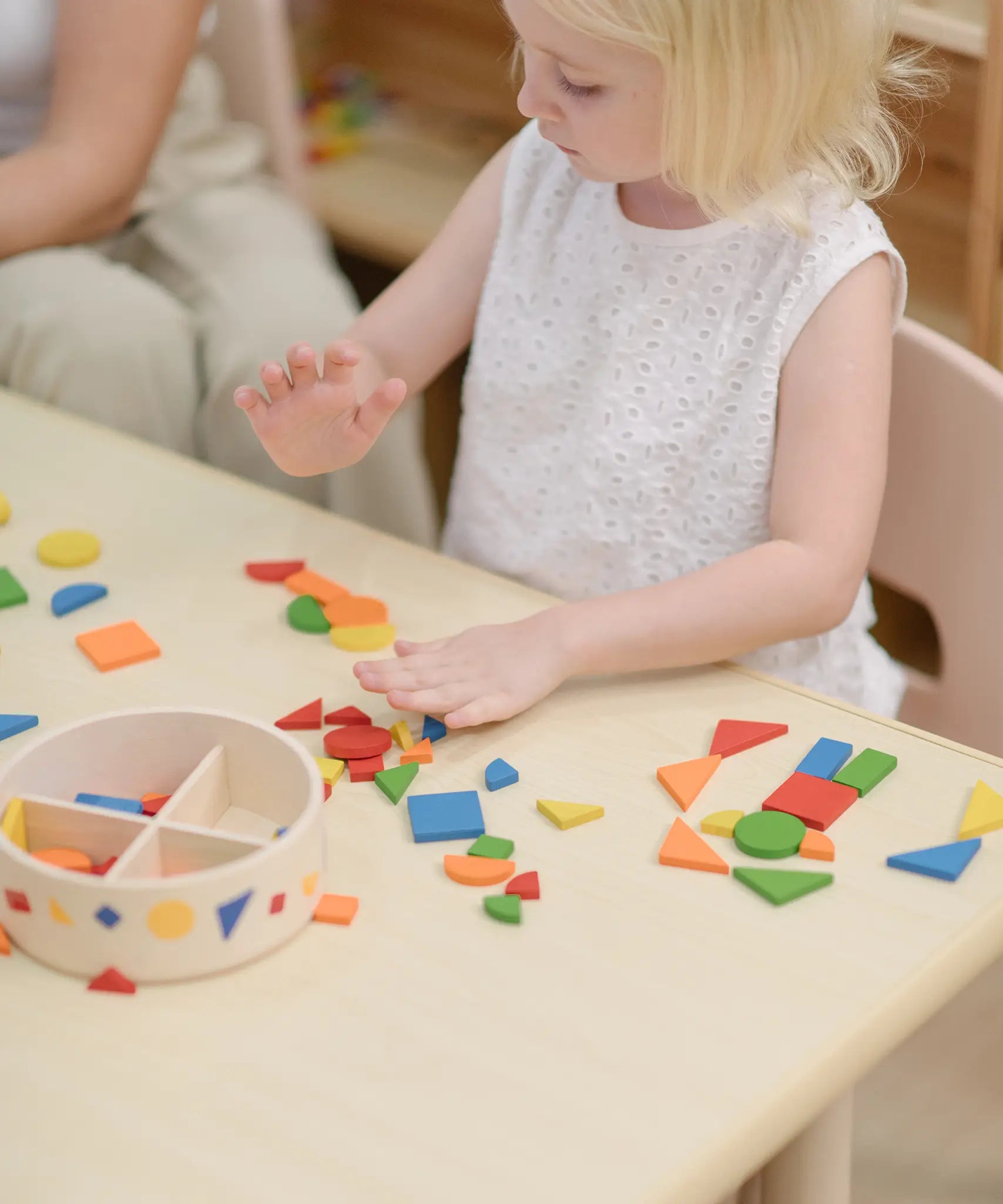 Child playing with the PlanToys mosaic wooden pattern making set taking the brightly coloured pieces out of the wooden storage tub.