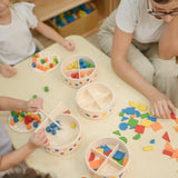 Children playing with the PlanToys mosaic wooden pattern making sets taking the brightly coloured pieces out of the wooden storage tub.