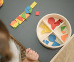 Overhead view of the wooden pieces from the PlanToys Mosaic wooden pattern making toy placed next to the wooden storage box.