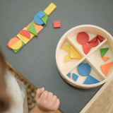 Overhead view of the wooden pieces from the PlanToys Mosaic wooden pattern making toy placed next to the wooden storage box.