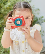 A child playing with a Plan Toys My First Camera, they are holding it up to their eye ready to snap away. 