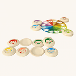 The PlanToys My Mood Memo game on a plain background. Some of the emotions discs are placed at the front some are upside down, showing the plain curved sides. The wheel of emotions can be seen in the background. 
