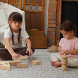 Two children sitting down on a patterned rug, one is playing with the PlanToys Hollow Blocks whilst the other is using the natural PlanToys stacker 